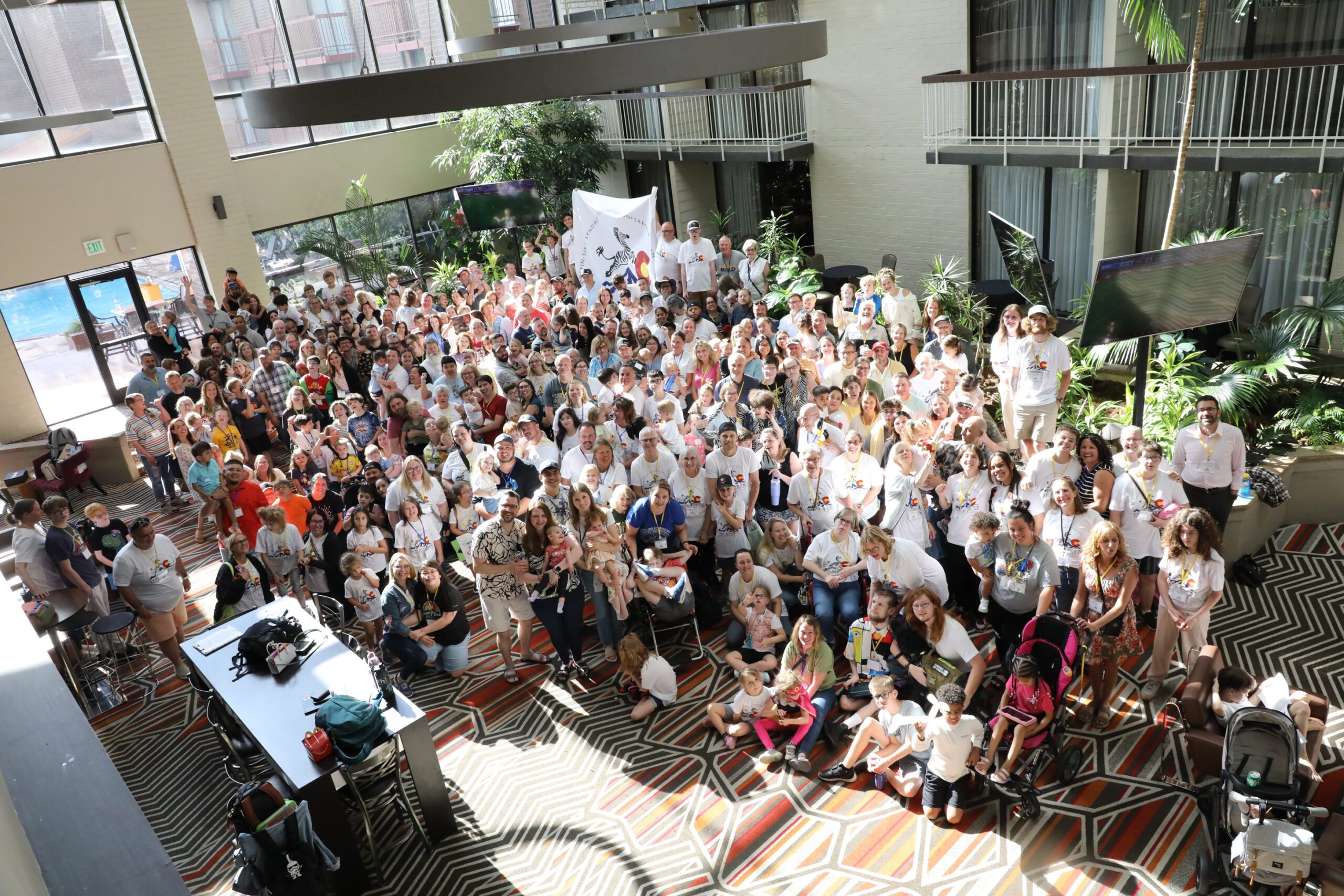 A large group of people gathered together for a group picture in the lobby of a hotel for the Coffin Siris Syndrome Foundation 2025 conference. 